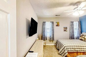 Ein Schlafzimmer mit Bett, Schreibtisch, Stuhl, Fernseher und Deckenventilator.