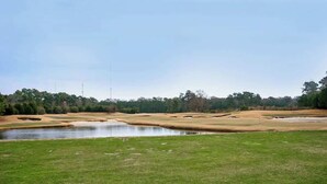 Un campo de golf con un estanque, búnkeres de arena y un cielo despejado.