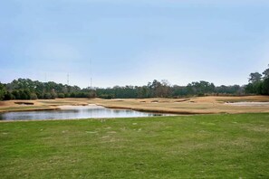 Ein Golfplatz mit Teich, Sandbunkern und blauem Himmel.
