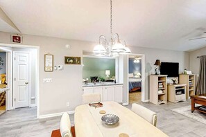 Ein Essbereich mit Tisch, Stühlen und einer Chandelier. Im Hintergrund befindet sich eine Küche mit Schränken und einer Arbeitsplatte.