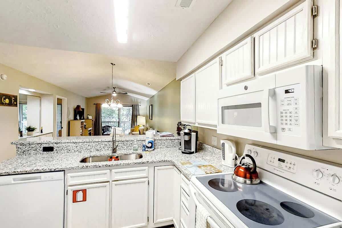 A kitchen with white cabinets, a granite countertop, a kettle, and a microwave.