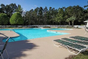 A swimming pool with a white fence, lounge chairs, and trees in the background. - Pinehurst Condos Unit 6J (Pawleys Island)