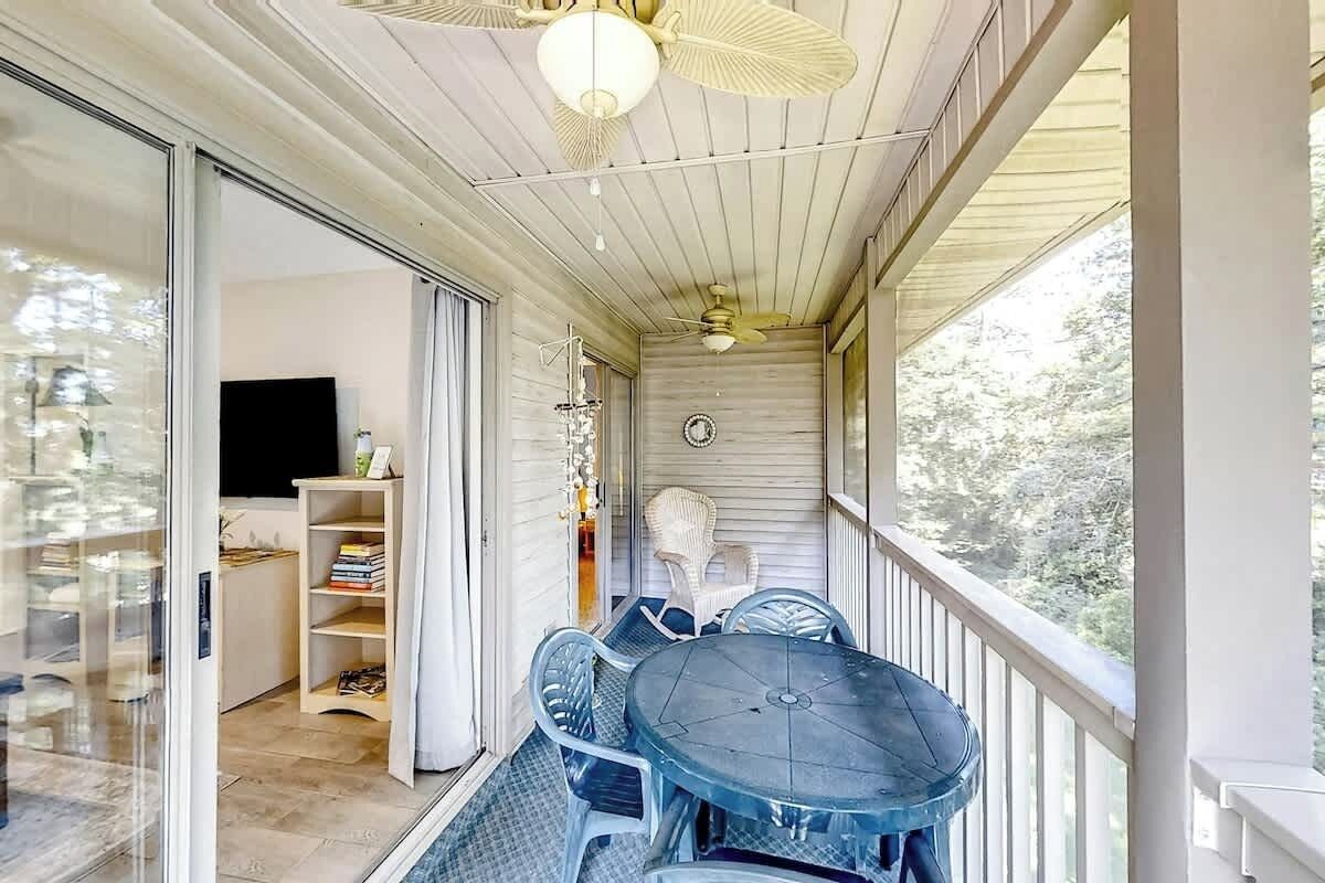 A covered balcony with a table and chairs, a ceiling fan, and a view of the outdoors.