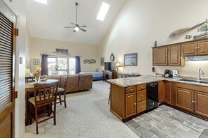 A spacious living area with a dining table, sofa, and kitchen with wooden cabinets and a dishwasher. - Golf Colony at Deerfield 26H (Surfside Beach)