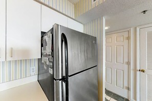 A stainless steel refrigerator in a kitchen with striped wallpaper and a white door in the background. - Beach Club III Unit 8-D (North Myrtle Beach)