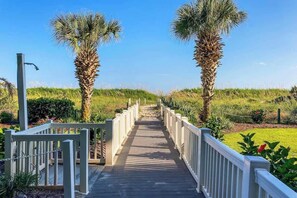 A wooden boardwalk leading to a beach with palm trees on either side. - Beach Club III Unit 8-D (North Myrtle Beach)