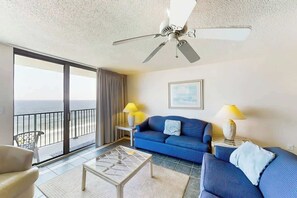 A room with a balcony, a blue sofa, a coffee table, and two lamps. - Beach Club III Unit 8-D (North Myrtle Beach)