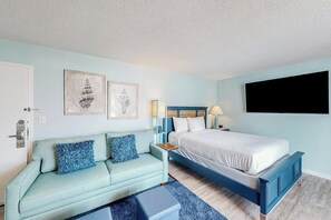 A bedroom with a bed, a sofa, a bedside table, and wall art. - Bay Watch Resort 0801 (North Myrtle Beach)