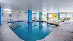 An indoor swimming pool with clear water, blue and white tiled walls, and a sunlit area with tables and chairs. - Bay Watch Resort 0801 (North Myrtle Beach)