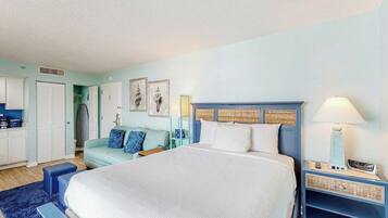 A bedroom with a large bed, a nightstand with a lamp, a wardrobe, and a small seating area with a sofa.