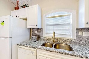 A kitchen with white cabinets, a granite countertop, a stainless steel sink, and a window with blinds.