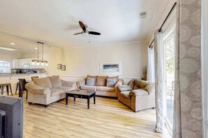A spacious living room with a ceiling fan, two sofas, a coffee table, and a kitchen in the background.