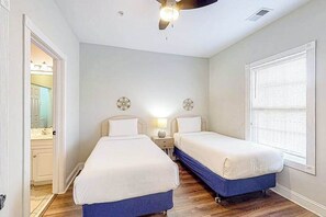 A bedroom with two beds, a ceiling fan, a window with blinds, and a door leading to a bathroom.