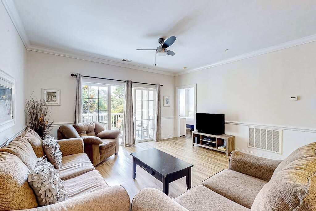 A spacious living room with a sofa set, a coffee table, a television, and a ceiling fan.