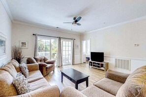 A spacious living room with a sofa set, a coffee table, a television, and a ceiling fan. - Magnolia North, Unit 202 (Myrtle Beach)