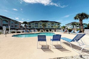 A pool area with lounge chairs and a building with multiple balconies in the background. - Magnolia North, Unit 202 (Myrtle Beach)