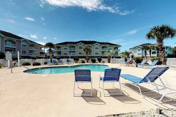 A pool area with lounge chairs and a building with multiple balconies in the background.