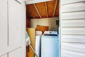 A compact laundry room with two stacked washers and dryers, a wooden ceiling, and a white exterior wall. - Flamingo House 1 - bottom (North Myrtle Beach)