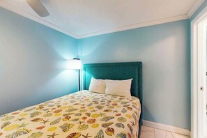 A bedroom with a teal headboard, a bed with a multicolored patterned bedspread, and a nightstand with a lamp. - Flamingo House 1 - bottom (North Myrtle Beach)