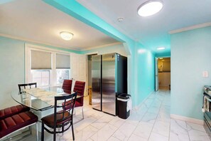 A dining area with a glass table and chairs, a refrigerator, and a trash bin. - Flamingo House 1 - bottom (North Myrtle Beach)