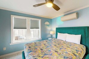 Une chambre à coucher comprenant un lit, un ventilateur de plafond, une fenêtre avec des stores et un climatiseur fixé au mur.
