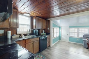 A kitchen with wooden cabinets, a dishwasher, and a window with blinds. - Flamingo House Retreat (North Myrtle Beach)