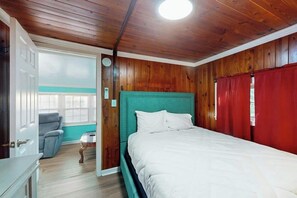 Ein Schlafzimmer mit Holzboden, einem Bett mit weißer Bettwäsche, einem türkisblauen Kopfteil und einem roten Vorhang.