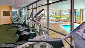 Ett gym med flera löpband och motionscyklar, stora fönster och utsikt över en utomhuspool.