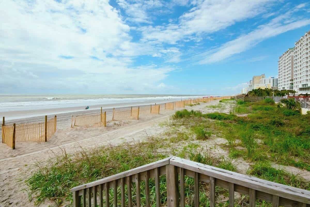 A beach with a wooden walkway leading to a building with multiple floors.