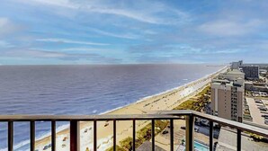 En vacker utsikt över kusten från en balkong med utsikt över en strand och havet, med byggnader i bakgrunden och en klar himmel.