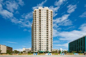 A tall, multi-story hotel with a central courtyard and a clear blue sky. - The Beach House at Palace Resort 1911 (Myrtle Beach)