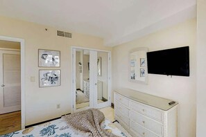 A bedroom with a bed, dresser, TV, and a door leading to another room. - The Beach House at Palace Resort 1911 (Myrtle Beach)