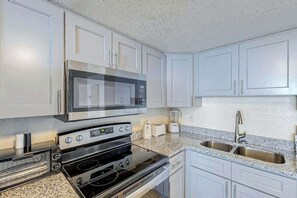 A kitchen with white cabinets, a stainless steel microwave, a stove, a toaster, and a sink. - Water's Edge Luxe | Nine Oh One (Murrells Inlet)