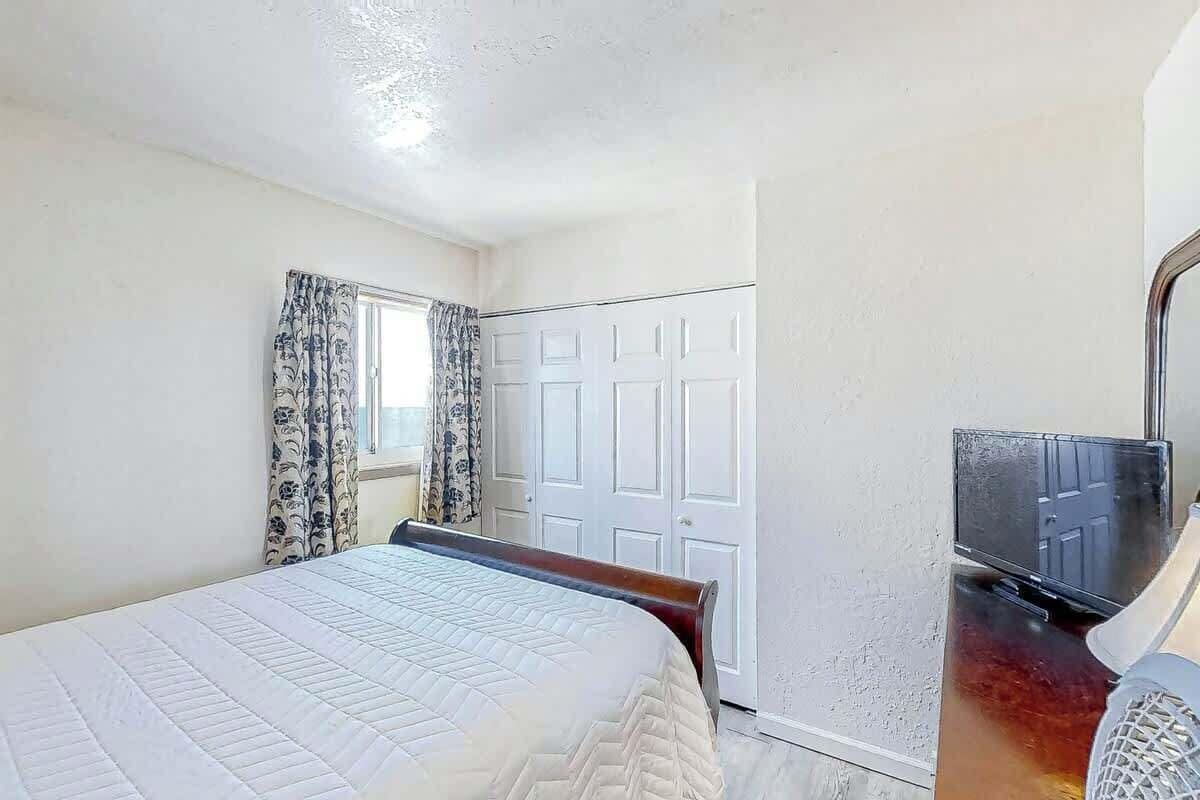 A bedroom with a bed, a wardrobe, a television, and a window with curtains.