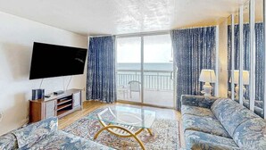 Una sala de estar con una televisión de pantalla plana, una mesa de centro de vidrio, un sofá y vistas al mar a través de amplios ventanales.