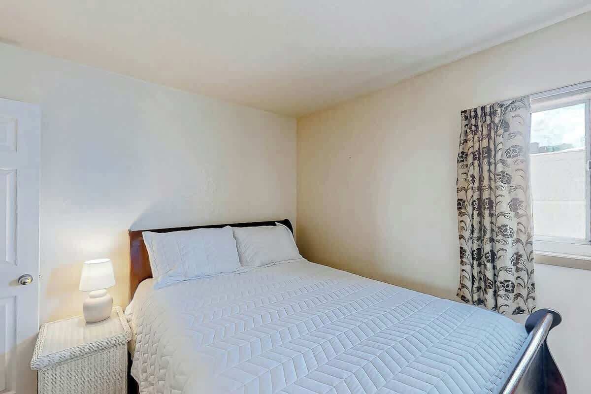 Une chambre à coucher avec un lit, une table de chevet, une lampe et une fenêtre avec des rideaux.