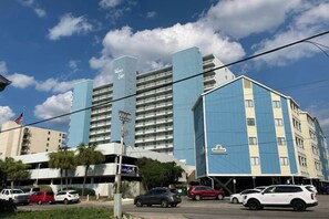 A hotel with multiple floors, a prominent sign, and a parking lot with several cars. - Water's Edge Luxe | Nine Oh One (Murrells Inlet)