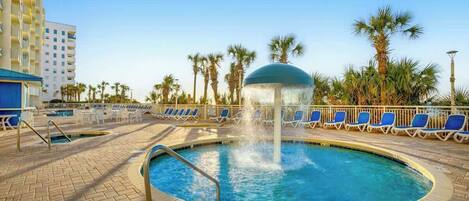 Ein Poolbereich mit einer Fontäne, Liegestühlen und Palmen.