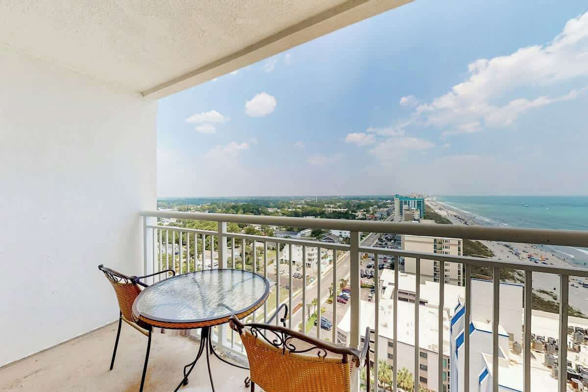 Un balcón con mesa y sillas, con vista a una playa y al horizonte urbano.