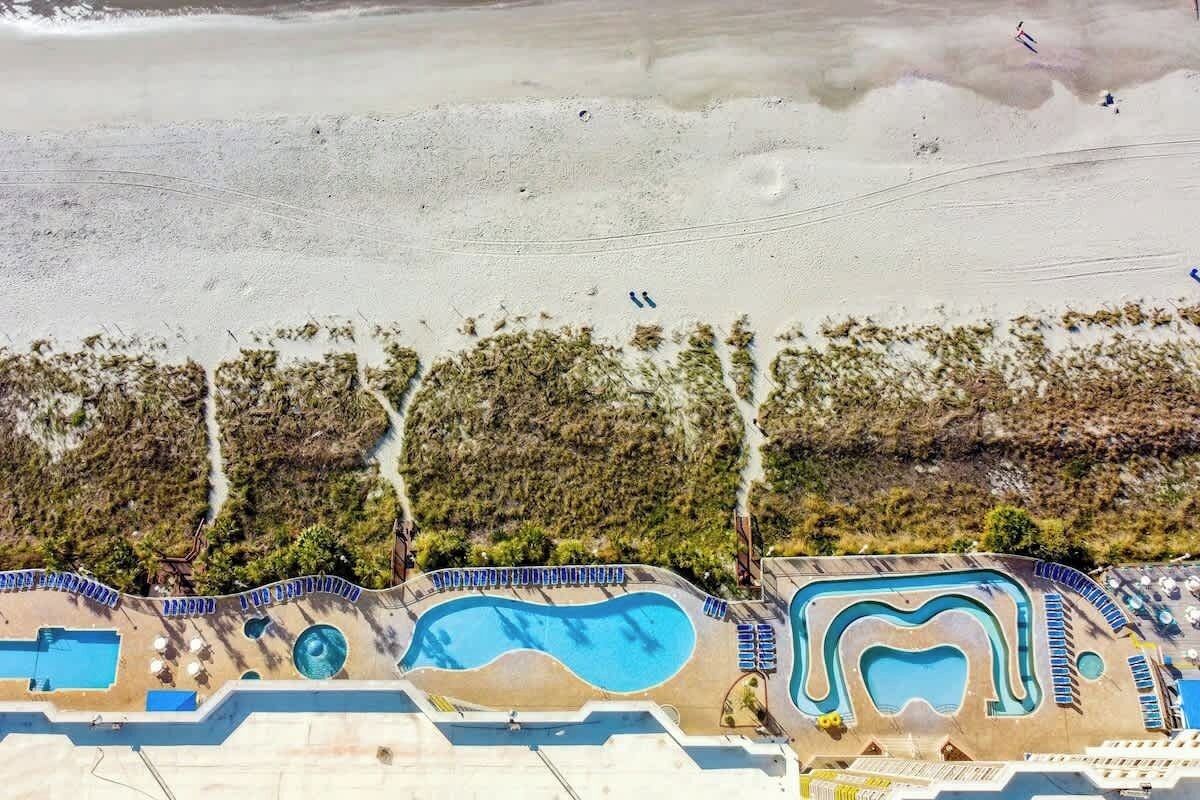 Un resort con varias piscinas, una zona de playa y montañas al fondo.