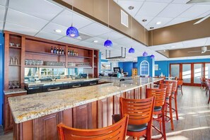 A bar area with a long counter, multiple stools, and a variety of bottles and glasses. - Bay Watch Resort 1901 (North Myrtle Beach)