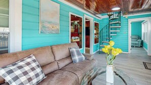A teal-walled room with a brown leather sofa, a glass coffee table, and a spiral staircase. - Flamingo House 2 - top (North Myrtle Beach)