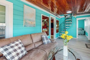 A teal-walled room with a brown leather sofa, a glass coffee table, and a spiral staircase. - Flamingo House 2 - top (North Myrtle Beach)