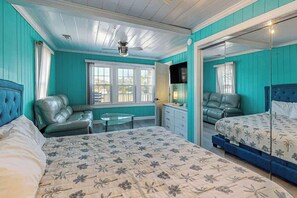 A room with teal walls, a bed with floral bedding, a sofa, a television, and a ceiling fan. - Flamingo House 2 - top (North Myrtle Beach)