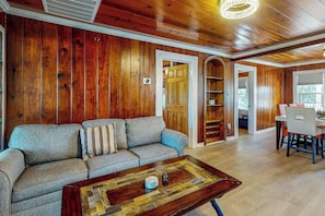 A living room with a sofa, coffee table, wooden walls, and a dining area with a table and chairs. - Flamingo House 2 - top (North Myrtle Beach)