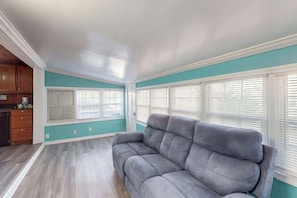 Ein Wohnzimmer mit grauem Sofa, türkisfarbenen Wänden und großen Fenstern mit Jalousien.