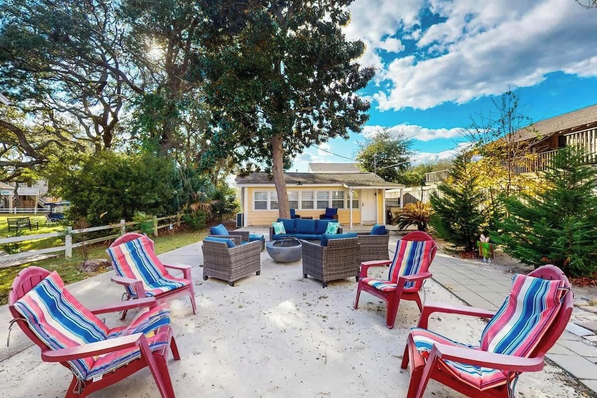 An outdoor seating area with wicker furniture and striped chairs, surrounded by trees and a building in the background.