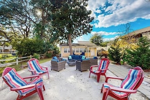 An outdoor seating area with wicker furniture and striped chairs, surrounded by trees and a building in the background. - Flamingo House 3 - courtyard (North Myrtle Beach)