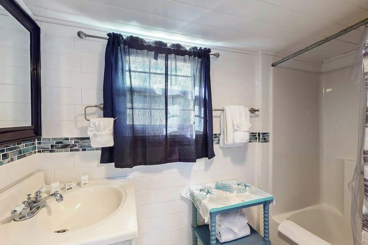 A bathroom with a sink, a small table with a towel, a shower, and a curtain.