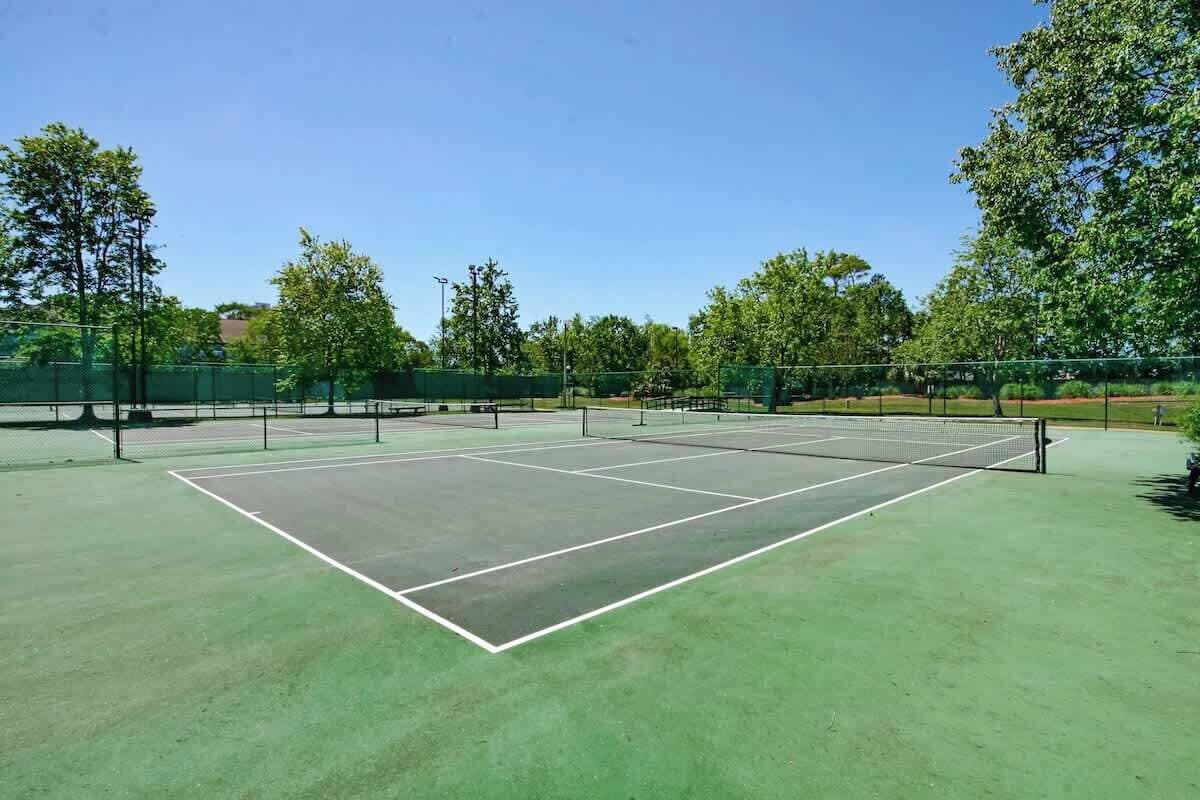 A tennis court with a net, surrounded by trees and a fence.